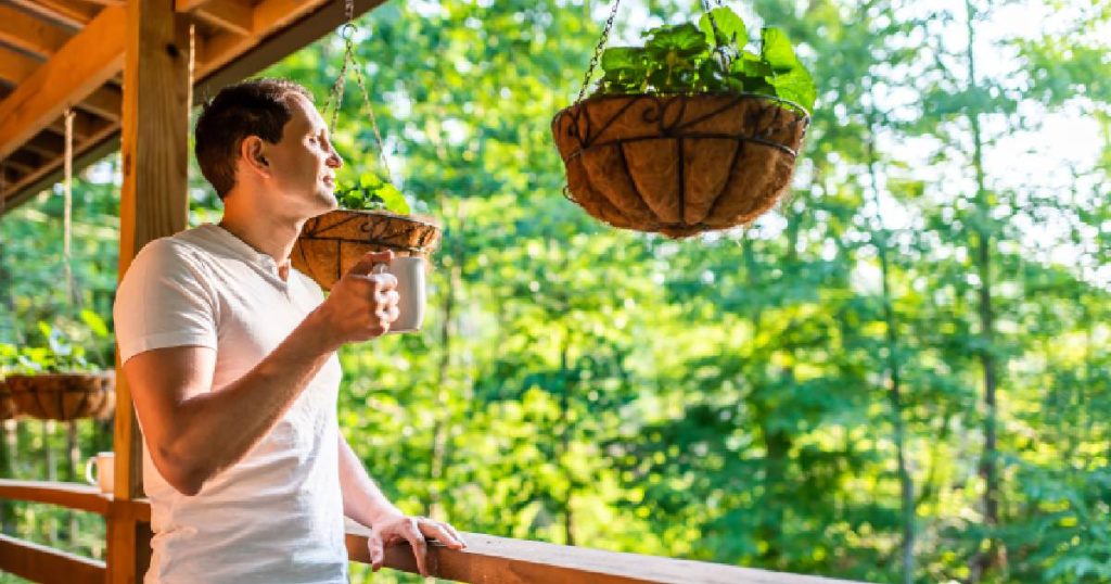 Een man geniet van een kopje warme drank op zijn volledig open veranda. Met een gesloten veranda zou zijn zicht op het bladerdek verstoord worden. Aan het dak van de veranda hangt een mandje met planten.