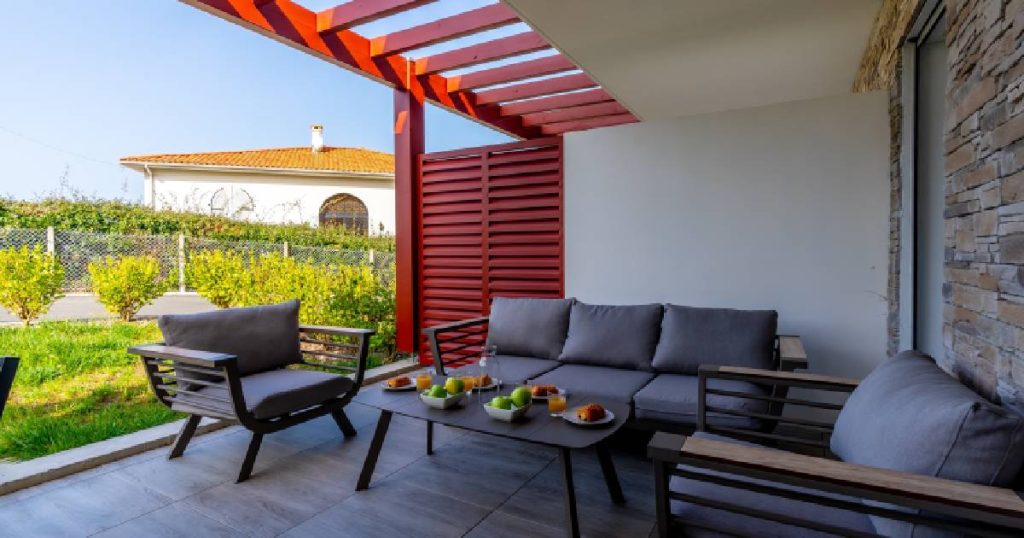 Een terrasoverkapping die uitgeeft op een tuin. Onder de overkapping staat een loungeset met zetels en een salontafel.