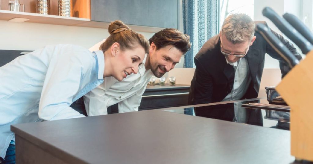 Een koppel bekijkt een showroommodel in hun zoektocht naar een goedkope keuken. Een keukenverkoper toont hen de keuken.