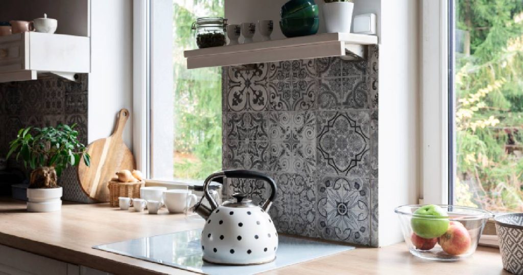 Detailbeeld van een relatief goedkope keuken in landelijke stijl met leuke keramieken tegeltjes. Het kunststof aanrecht met houtlook, het houten keukengerei en de witte wandplankjes geven de keuken een sfeervolle en authentieke look - voor een zachte prijs.