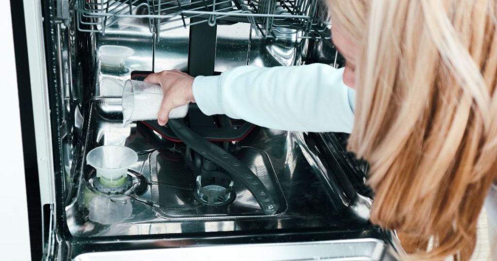 Een dame giet zout voor de vaatwasser via een trechter in het reservoir binnenin de vaatwasmachine.