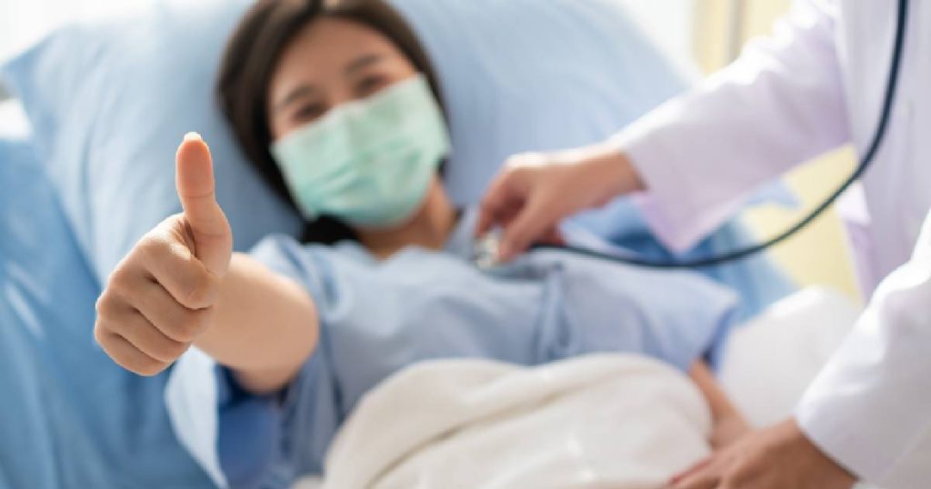 Een dame in een ziekenhuisbed steekt haar duim op terwijl een arts haar onderzoekt: ze hoeft dankzij haar hospitalisatieverzekering niet in te zitten met hoge kosten voor een ziekenhuisopname.