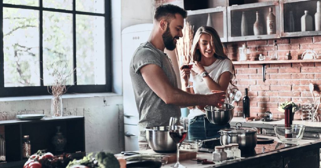 Een man en vrouw koken in een industriële keuken met houten elementen, zichtbare bakstenen muur en stoere metalen accenten.