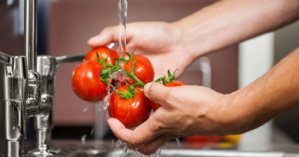 Twee handen spoelen een tros tomaten onder een kraan in de spoelzone van een keuken met ergonomische inrichting.