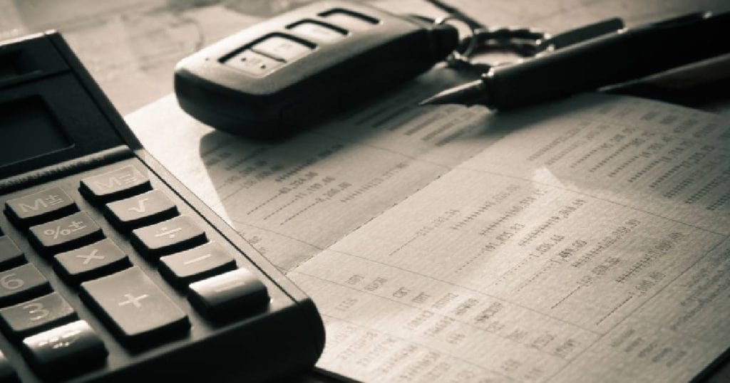 Het aanvraagformulier voor het inschrijvingsbewijs van een nieuwe auto, een vulpen, autosleutels en rekenmachine op een tafel.