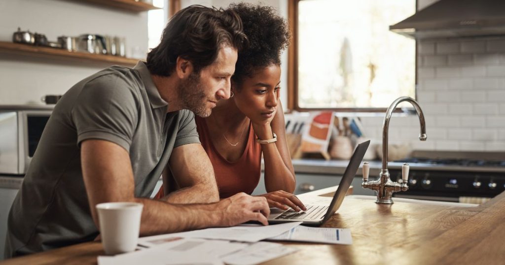 Een koppel zit in de keuken aan een laptop voor het ontwerp, de inrichting en de budgettering van hun keuken.