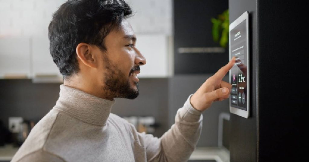 Een man bedient een touchscreen in een zwarte keuken die werd ontworpen volgens de laatste keukentrends.