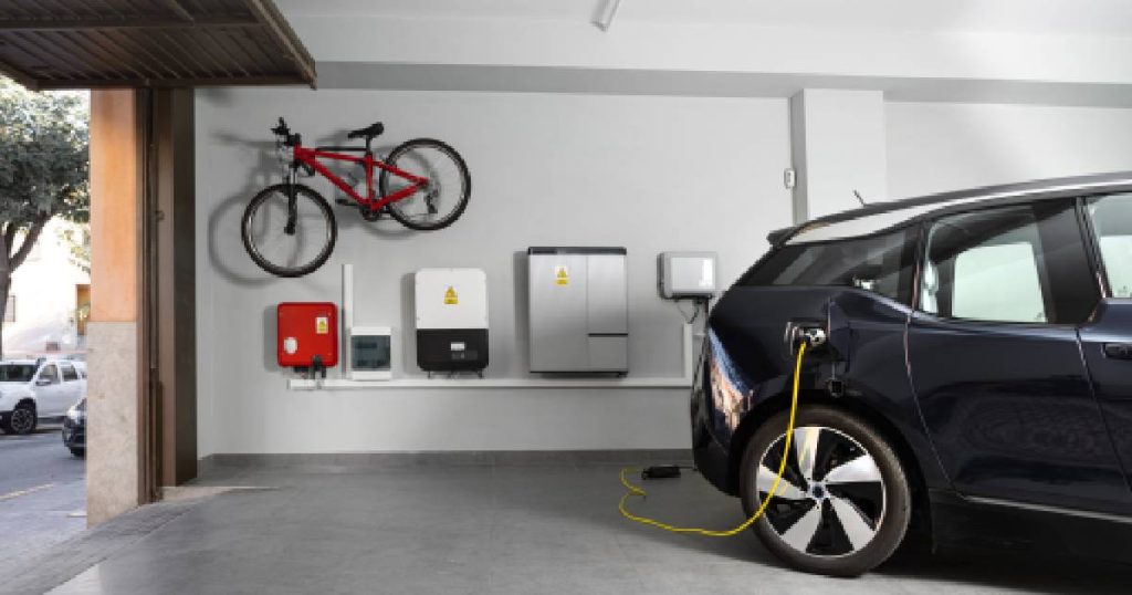 Een zwarte elektrische wagen in een garage van een woning waar men thuis een laadpaal heeft laten installeren. Een gele kabel verbindt de blauwe auto met het laadpunt.