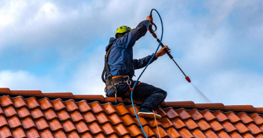 Een dakwerker sproeit een nieuwe coating op betonnen dakpannen om hun levensduur te verlengen en de pannen te beschermen tegen vocht.