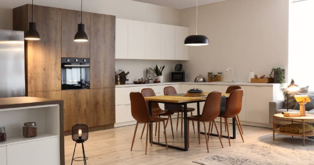 Een mooie moderne open keuken met greeploze witte en houten keukenkasten, warm witte muren, een houten vloer en een gezellige eettafel met karamelbruine stoelen.