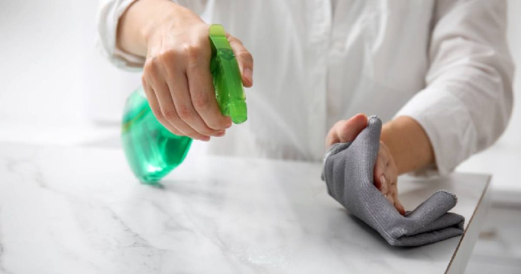 Twee handen in een wit hand maken een natuursteen keukenblad uit marmer schoon met een zachte doek en mild reinigingsmiddel.