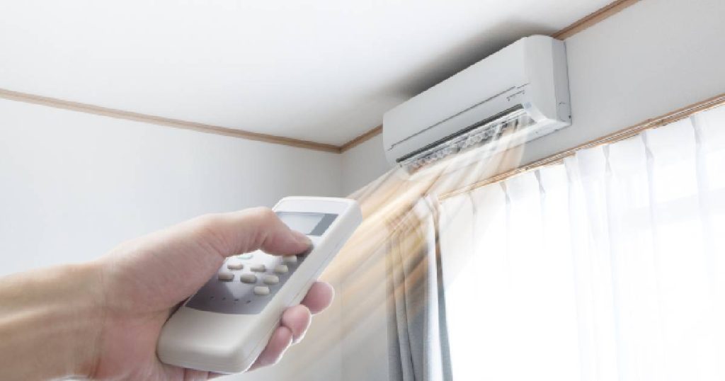 Een hand gebruikt een afstandsbediening om een airco in te schakelen die de lucht ontvochtigt bij het verwarmen.