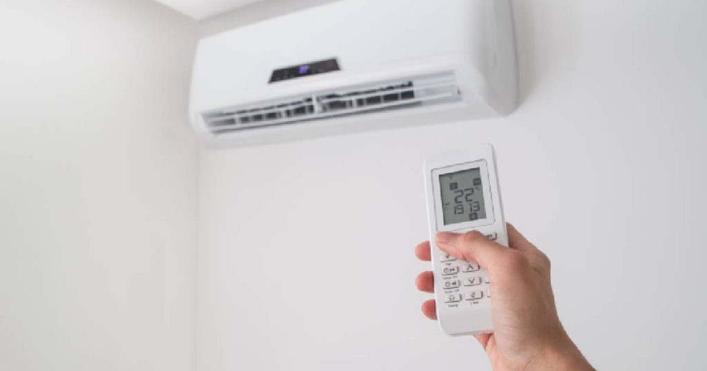 Een afstandsbediening van een airconditioning binnenunit in een hand, met een scherm waarop weergegeven wordt in welke mate de airco ontvochtigt bij het verwarmen en koelen van de ruimte.