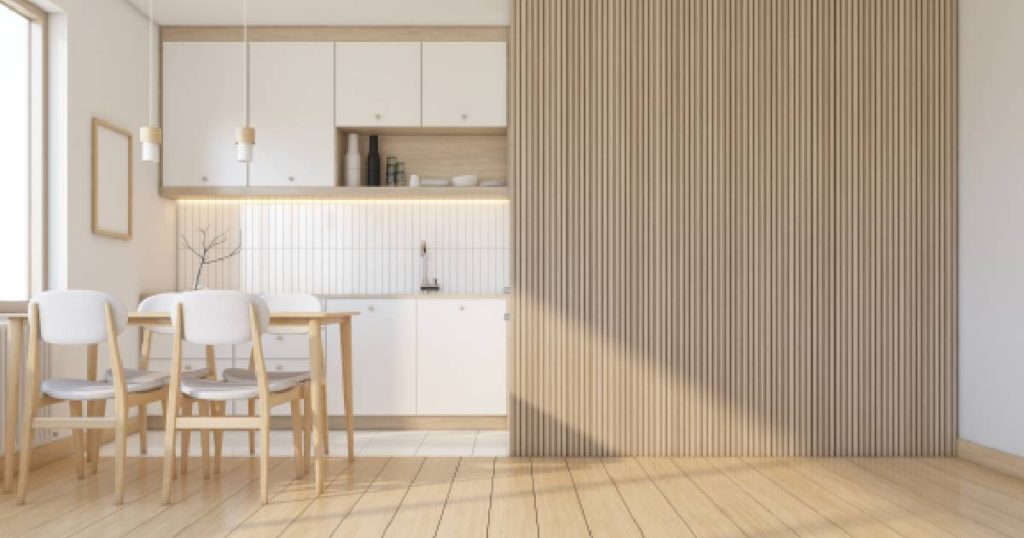 Een oude keuken in Japanse stijl na het pimpen: een houten lattenwand werd toegevoegd voor een natuurlijke uitstraling en betere akoestiek in de keuken. De keuken beschikt over een houten vloer, wit met houten keukenkastjes, een wit betegelde spatwand en een houten eettafel met houten stoelen met witte leuning en zitvlak.