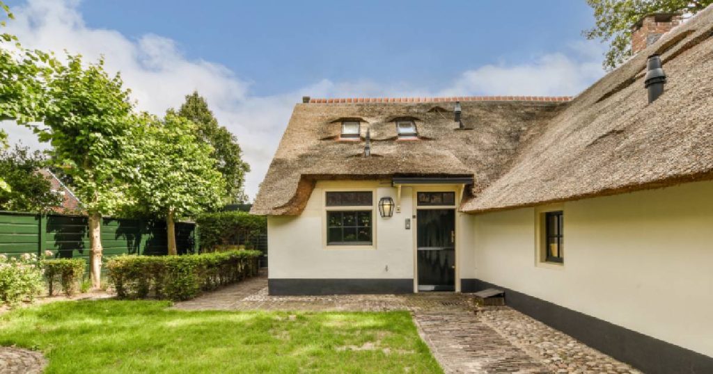 Een rieten dak op een woning met lichtgele gevel met donkergrijze onderrand.