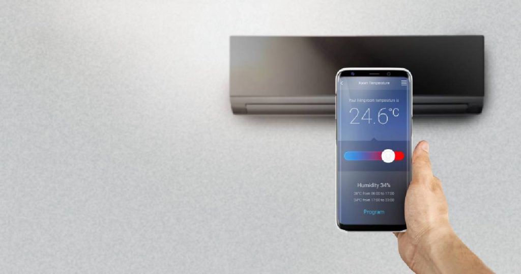 Een smartphone met SmartThings van Samsung, een applicatie waarmee je een Samsung airco kunt bedienen door de gewenste temperatuur in te stellen en de luchtvochtigheid te regelen. Op de achtergrond een stijlvolle zwarte Samsung Windfree airco in wandmodel: een kwalitatief toestel voor een eerlijke prijs.