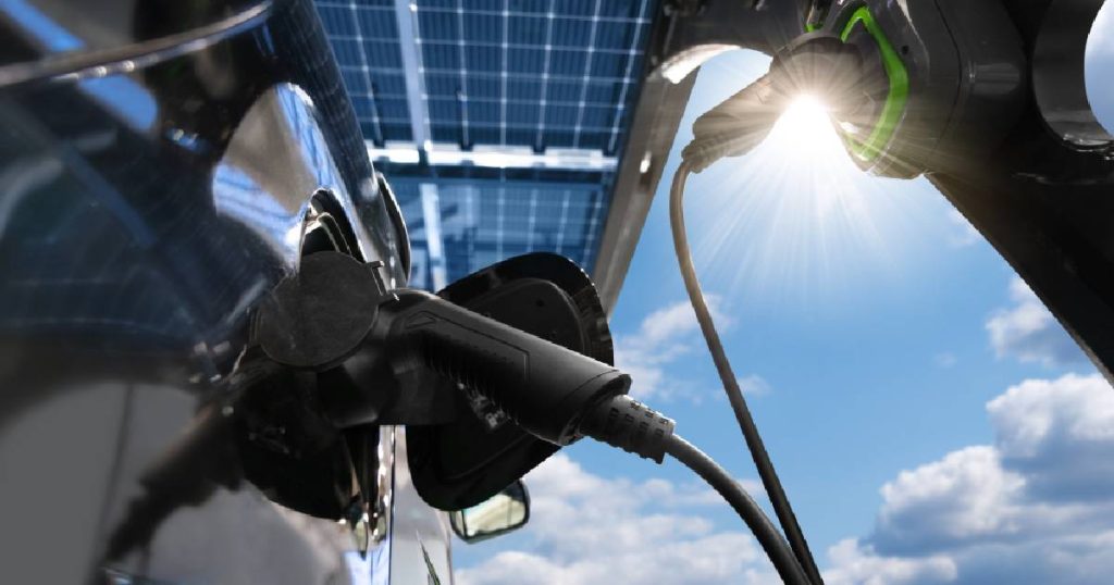 Een elektrische wagen aangesloten op een slimme laadpaal en geparkeerd onder een carport met zonnepaneeldak.