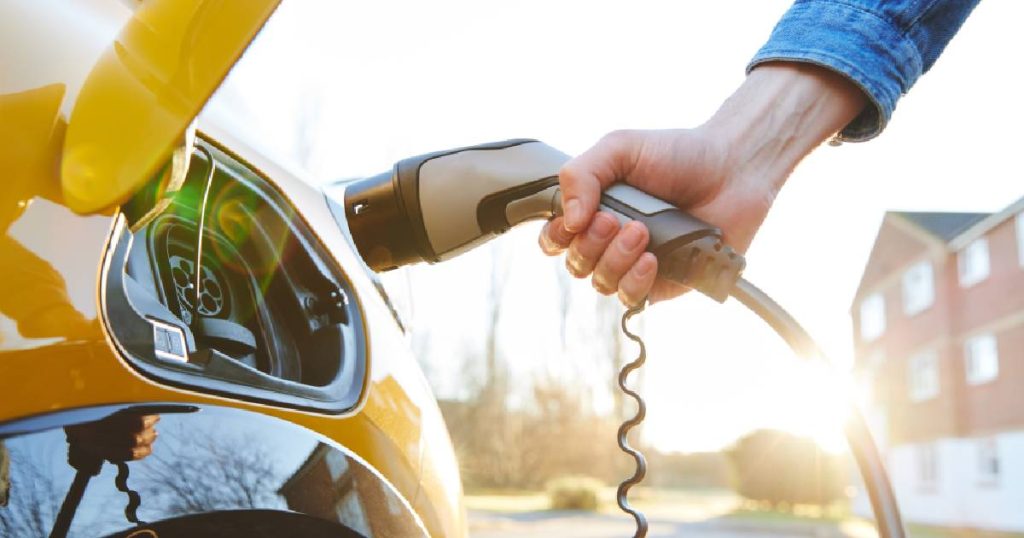 Een gele elektrische auto en een laadkabel van een snelle laadpaal voor thuis in de handen van een persoon met jeansjasje. 