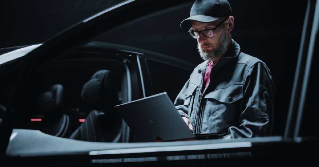 Een expert in elektrische voertuigen staat naast een elektrische auto met geopende deur en informeert zich via een laptop naar de verschillende soorten laadpalen.