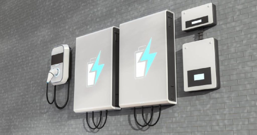 Een thuisbatterij, wallbox laadpaal en omvormers tegen een grijze, bakstenen gevel: een systeem met een vrij hoge prijs, maar een goede oplossing voor wie zoveel mogelijk van de zelfopgewekte zonne-energie wilt verbruiken. 