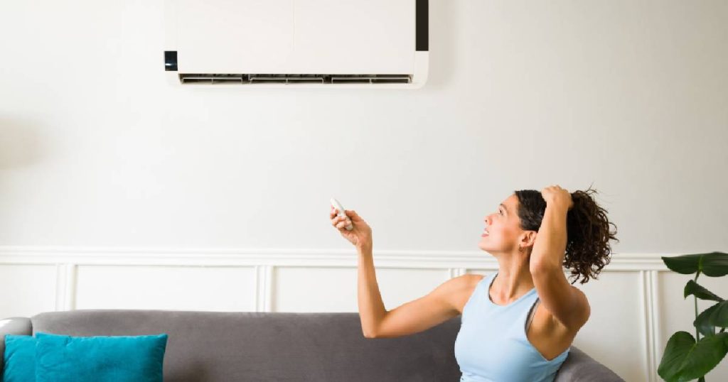 Een dame gebruikt de afstandsbediening om haar airco in te stellen op een warme zomerdag. Ze houdt het verschil tussen de temperatuur op de airco  en de temperatuur buiten zo klein mogelijk: dat is energiezuiniger en gezonder.