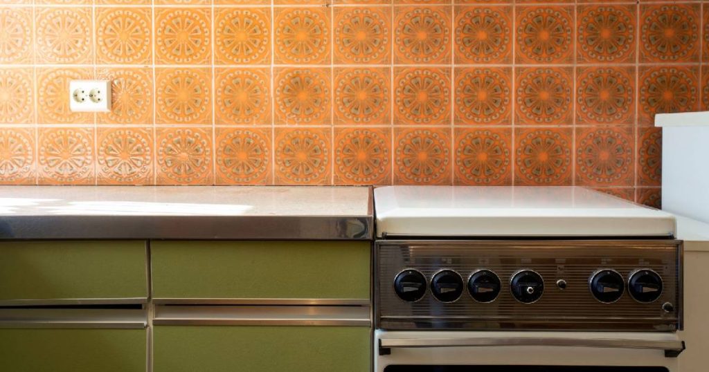 Een authentieke vintage keuken met bruin met oranje wandtegels, rokerig groene keukenfronten en een retro oven. Het interieur doet sterk aan de jaren '70 denken.