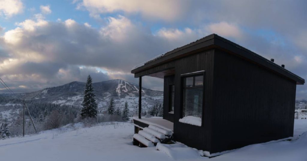 Een klein gebouwtje met lessenaarsdak op een berg in een winters landschap.