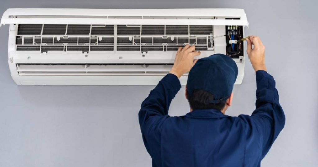 Ongeacht wat een Mitsubishi Electric airco systeem kost: een goede installateur is van onschatbare waarde. Een installateur in blauwe overall met blauwe pet installeert hier een grote witte airco wandunit.