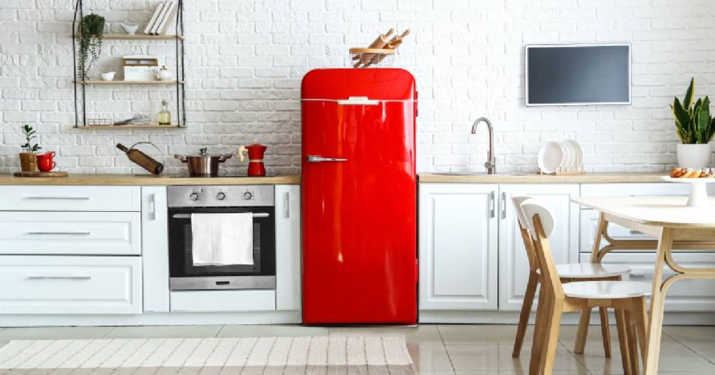 Een overwegend witte keuken met een koelkast in een sterk contrasterende rode kleur. Het rood komt terug in de percolator en de koffiekopjes. 