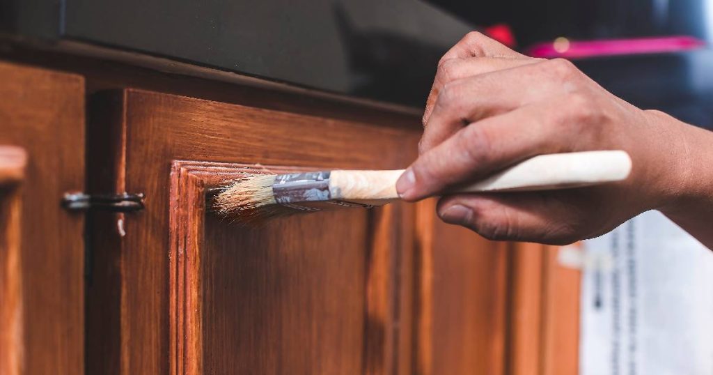 Een dame is zelf haar keuken aan het renoveren: ze bekleedt de houten keukenkastjes met een nieuw laagje vernis.